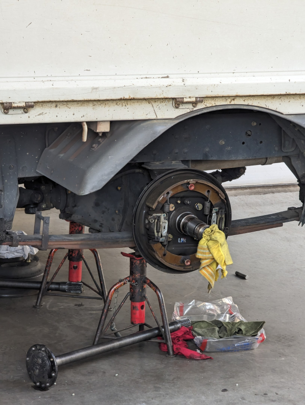 Ein gelber, tuchbedeckter Lastwagen in einer Garage mit Werkzeugen und Gegenständen, die vor ihm auf dem Boden verstreut sind.