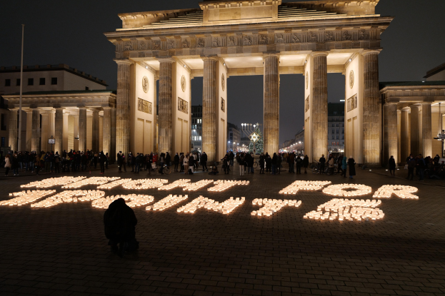 Gruppe von Menschen, die vor dem beleuchteten Brandenburger Tor in Berlin, Deutschland, mit "Kampf um Freiheit" auf dem Boden stehen.