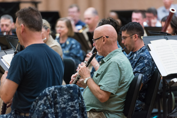Eine Gruppe von Männern, die Klarinetten in einem Raum mit Notenständern vor sich spielen.