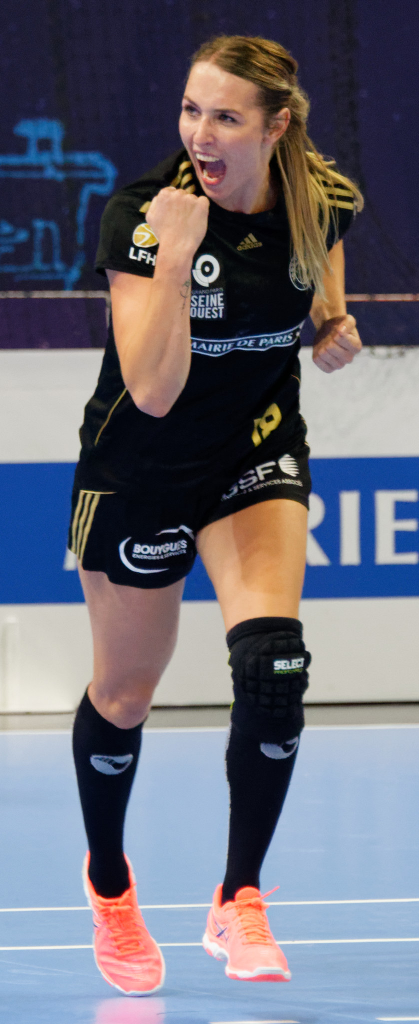 Eine Frau in schwarzem Shirt und Shorts spielt Volleyball auf einem Feld, mit einem Banner im Hintergrund.