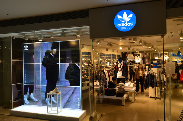 Ein Adidas-Laden in einem Einkaufszentrum mit Schaufensterpuppen, Kleidung an Bügeln, Schuhe auf Ständern und beleuchteter Laden mit einem Schild mit dem Adidas-Logo, das auf die Adidas Originals-Marke hinweist.