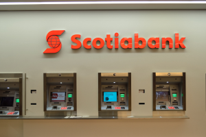 Ein modernes Scotiabank-Geldautomatengerät in Schwarz und Silber mit einem großen Bildschirm und mehreren Tasten, das vor einer hellgrauen Wand mit gerahmten Bildern und der Aufschrift "Schottische Bank" im Hintergrund positioniert ist.