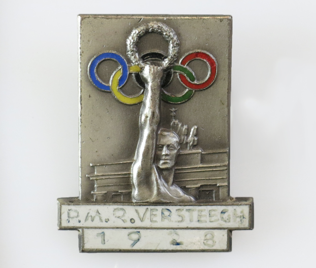Eine silberne olympische Medaille mit den olympischen Ringen und der Aufschrift "Olympische Spiele" wird von jemandem in der Hand gehalten.