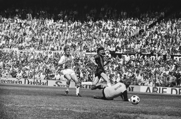 Schwarzes und weißes Foto von Männern, die auf einem Feld Fußball spielen, mit Zuschauern im Hintergrund und einer 'Bundesliga 1978-79 Ajax 1-1 Hannover 96' Fahne.