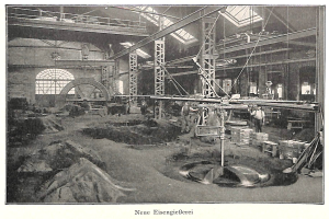 Ein altes Schwarz-Weiß-Foto einer Fabrik mit Menschen, die an einer Maschine arbeiten, umgeben von Metallstangen und -pfählen, mit Text unten: "Neue Eisenglebeerei, die erste Fabrik Deutschlands."