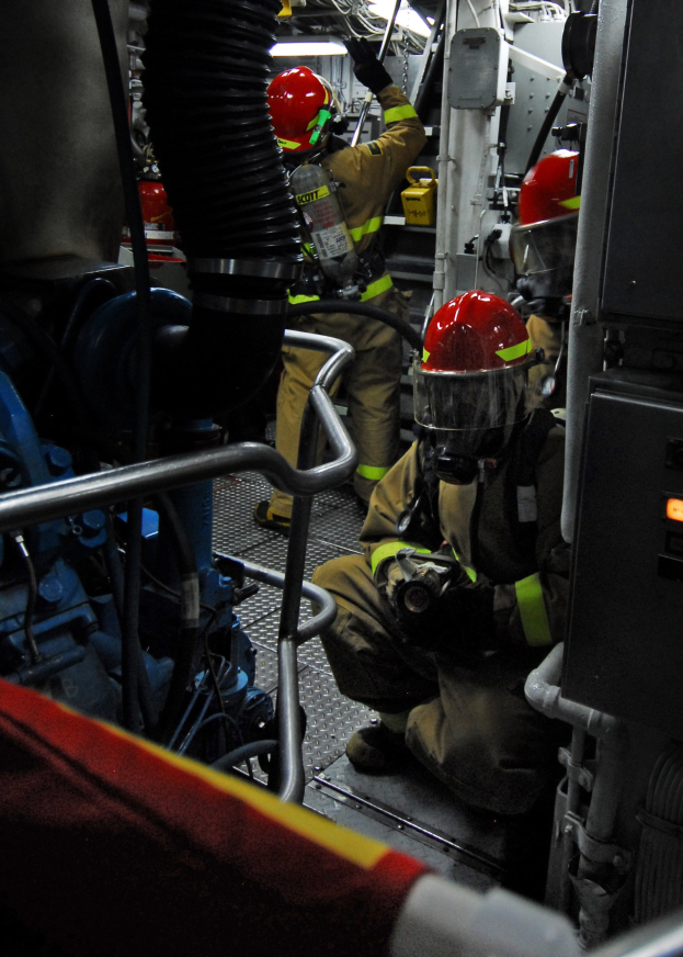 Feuerwehrleute in Schutzausrüstung an einem Löschfahrzeug mit Equipment im Hintergrund und einer Lampe oben.