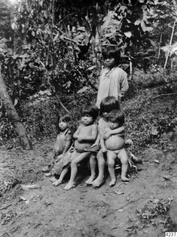 Fünf Kinder sitzen auf einer Schotterstraße in einem Schwarz-Weiß-Bild mit Bäumen und einer stehenden Person im Hintergrund; Text erscheint unten.