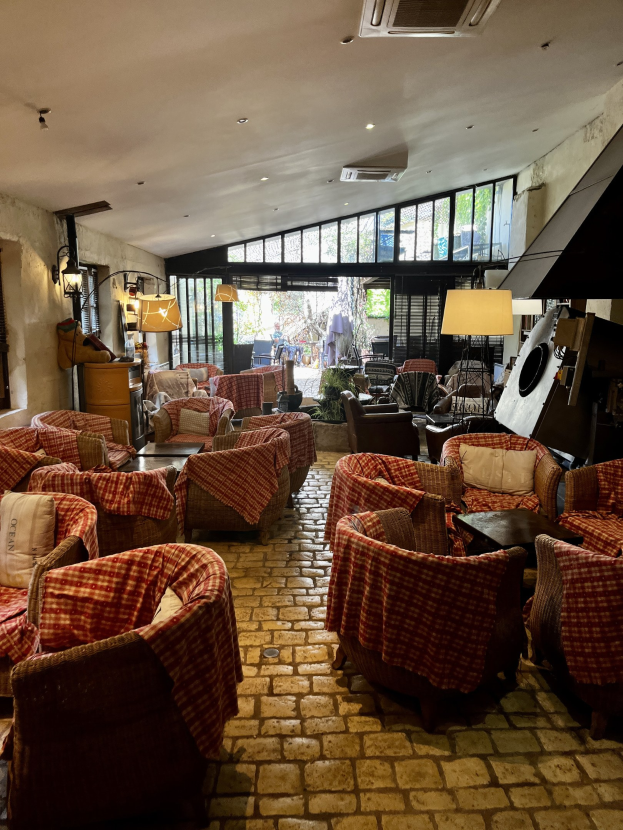 Eine geräumige Lobby mit zahlreichen Stühlen, Tischen, Sofas mit Kissen, Wandlampen, einer Deckenklimaanlage und großen Glasfenstern an der Rückseite.