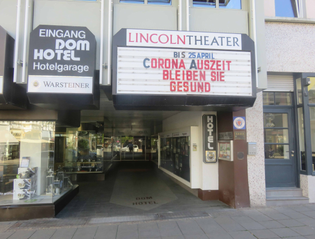 Außenansicht des Lincoln Theaters in Berlin, Deutschland, mit Glasfenstern und -türen sowie einer Texttafel und einem Inneren, das eine pulsierende Stadtlandschaft vermuten lässt.