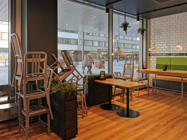 Ein Restaurant in Berlin mit Holztischen und Stühlen vor einem großen Fenster, das Fußgänger, Gebäude und Straßenelemente zeigt.
