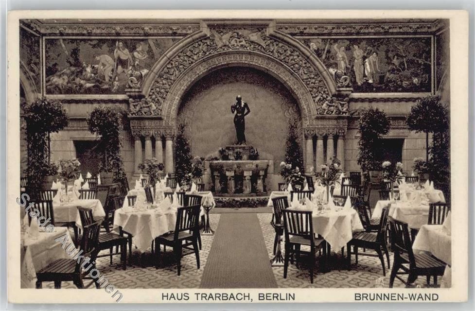 Schwarzes und weißes Foto eines alten Berliner Restaurant-Interieurs mit Tischen, Stühlen, Blumenvasen, einer Statue, Wandskulpturen, Pflanzen und Text unten.
