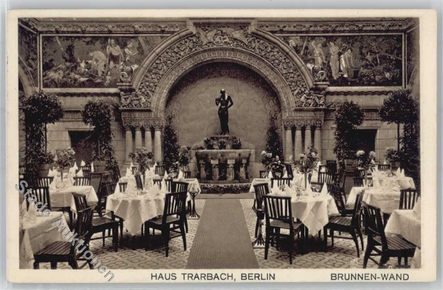 Schwarzes und weißes Foto eines alten Berliner Restaurant-Interieurs mit Tischen, Stühlen, Blumenvasen, einer Statue, Wandskulpturen, Pflanzen und Text unten.