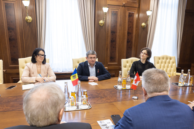 Gruppe von Menschen in einem formellen Setting um einen Holztisch mit EU-bezogenen Gegenständen, die in eine Diskussion vertieft sind.