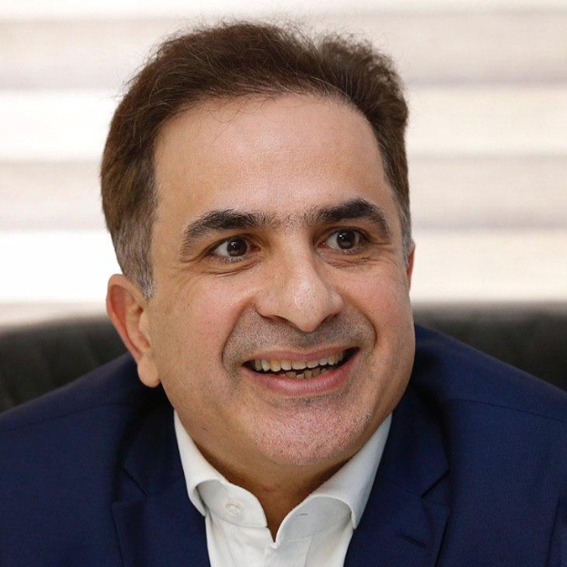 Ein Mann im blauen Anzug lächelt in die Kamera und scheint über seine jüngste Ernennung zum neuen CEO zu sprechen, mit einem unscharfen Hintergrund.