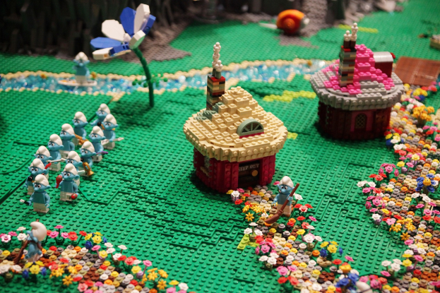 Ein Lego-Modell einer Kleinstadt mit Häusern, Blumen, Spielzeugen, Pflanzen und anderen Gegenständen, mit einem leicht unscharfen Hintergrund, der einen träumerischen Effekt erzeugt.