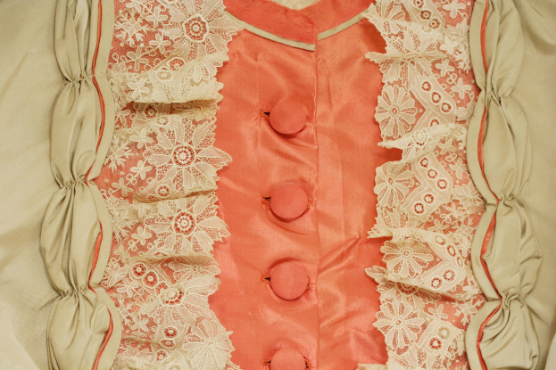 Nahaufnahme eines rosafarbenen und cremefarbenen Kleides mit weißer Spitzenverzierung und Frontknöpfen, das eine klassische und elegante Gestaltung aufweist.