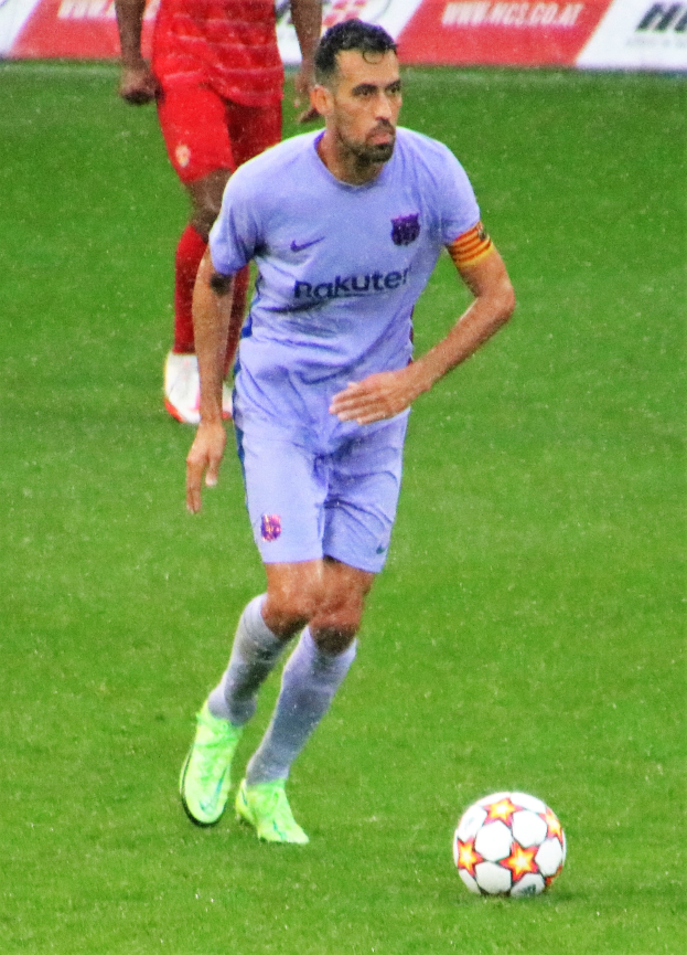 Ein Fussballspieler in einem Sportdress und -schuhen ist im Einsatz auf dem Feld, mit einer Texttafel im Hintergrund.