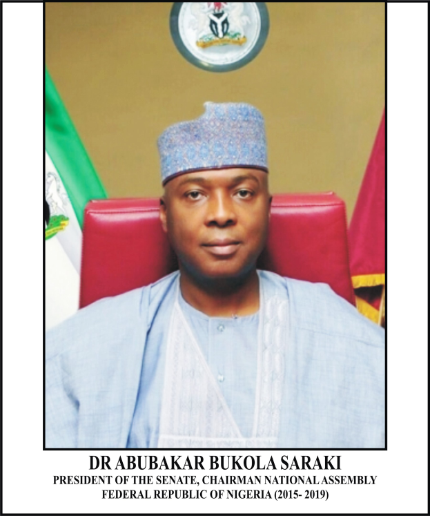 Dr. Abubakar Bukola Saraki, President of the Senate, seated in a chair wearing a blue dress and cap, with two flags and a logo on the wall behind him, and a framed nameplate at the bottom.