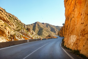 Winding road through a rocky gorge with hills on either side under a clear blue sky.