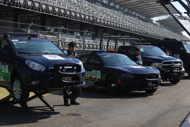 Polizeifahrzeuge vor einer Rennstrecke geparkt, uniformierte Personen auf der Straße stehend, Stadion und Absperrungen im Hintergrund