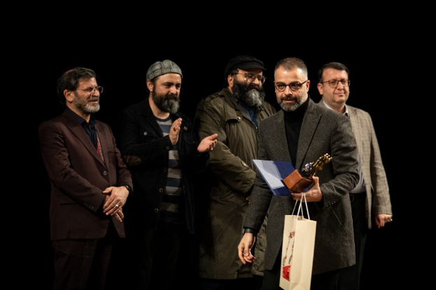 Eine Gruppe von Männern steht auf einer Bühne bei Nacht, einer hölt eine Tasche und eine Trophäe und feiert die Eröffnung des Berliner Filmfestivals.