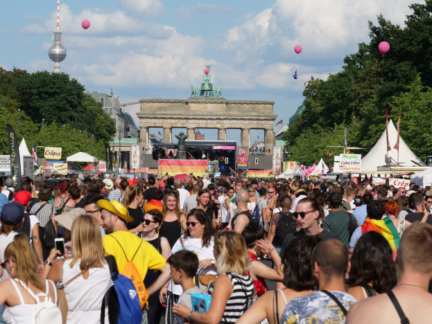 Eine große Menschenmenge steht vor dem Brandenburger Tor in Berlin, Deutschland, viele tragen Mützen und Schutzbrillen, einige halten Mobiltelefone, mit Zelten, Plakaten, Bäumen und Gebäuden im Hintergrund, unter einem bewölkten Himmel mit Ballons.