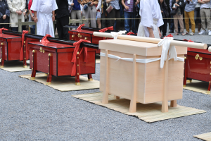 Eine Gruppe von Menschen steht um eine Reihe von Holzsärgen auf dem Boden, einige halten Kameras und Mobiltelefone, im Hintergrund ist ein Seilzaun zu sehen, der auf eine Grabkammer hindeutet.