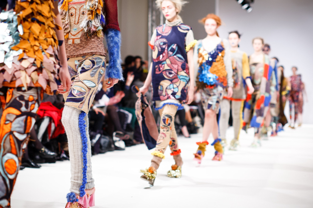 Eine Gruppe Von Frauen Geht Den Laufsteg Bei Der London Fashion Week Herunter, Mit Verwischten Zuschauern Und Heller Beleuchtung, Die Ein Traumhaftes Effekt Schaffen.