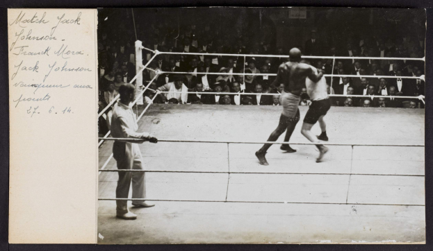 Schwarz-weiß-Foto von zwei Boxern, einem Ringrichter und Zuschauern in einem Boxring, mit dem Text "Jack Johnson vs Frank Morgan" in der oberen linken Ecke.