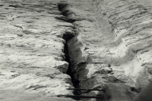 Ein Schwarz-Weiß-Foto eines großen Risses im Boden, wahrscheinlich ein Entwässerungsgraben, mit einem sichtbaren Wasserzeichen auf der linken Seite.