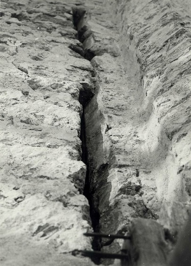Ein Schwarz-Weiß-Foto eines großen Risses im Boden, wahrscheinlich ein Entwässerungsgraben, mit einem sichtbaren Wasserzeichen auf der linken Seite.
