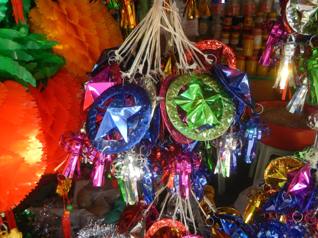 Farbenfrohe Dekorationen wie Laternen, Bänder und Flaschen hängen von einer Decke über Regalen in einer festlichen Umgebung.