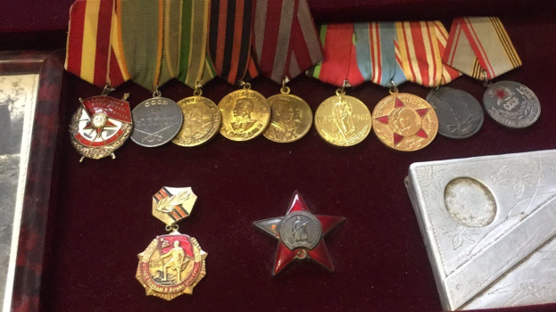 Eine hölzerne Kiste mit verschiedenen Medaillen, darunter ein roter Stern als Symbol der Sowjetunion, ordentlich angeordnet mit einem zusätzlichen Objekt auf der rechten Seite.