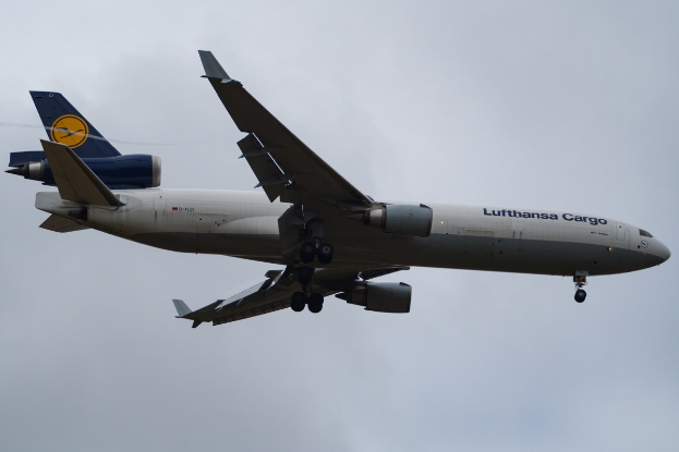 Ein Lufthansa Cargo Boeing 777-300ER im Flug, mit ausgebreiteten Flügeln und aktivierten Triebwerken, mit sichtbarem Text auf dem Rumpf gegen einen bewölkten Himmel.