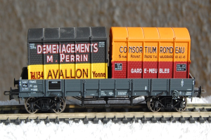 Ein Spielzeug-Zugwaggon mit Text darauf steht auf einer schneebedeckten Schiene, mit einer Wand im Hintergrund.