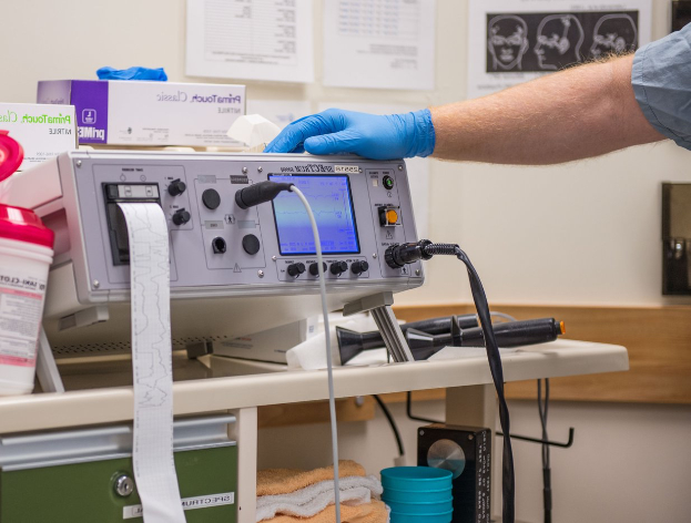 Eine Person in blauen Handschuhen arbeitet an einem medizinischen Gerät an einem unordentlichen Tisch in einer Krankenhausumgebung.