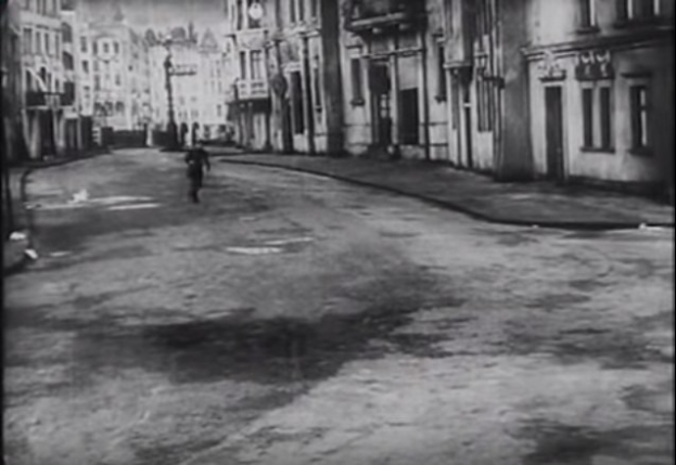 Schwarz-weiß-Foto eines Mannes, der eine von hohen Gebäuden gesäumte Stadtstraße entlanggeht.