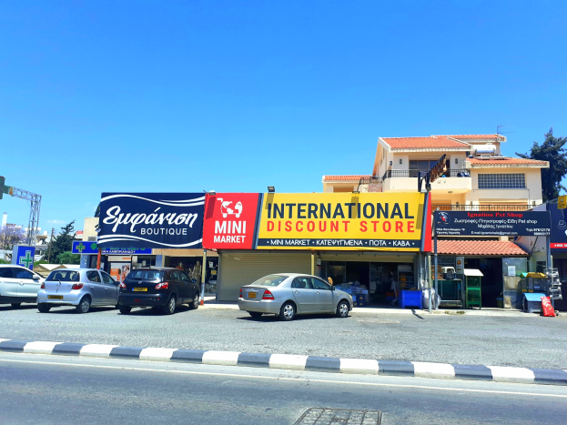 Internationaler Discounter an einer Straßenecke mit umliegenden Gebäuden, Fahrzeugen, Verkehrszeichen, Straßenmöbeln, Bäumen und einem klaren blauen Himmel.