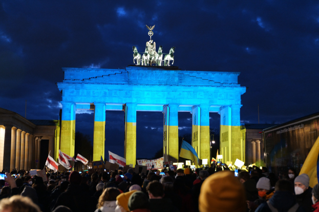 Menschenmenge mit Fahnen und Plakaten vor dem Brandenburger Tor, mit einer Fahne auf der rechten Seite.
