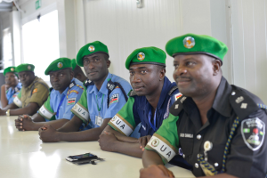 Gruppe von Polizeibeamten, die an einem Tisch während einer Schulung sitzen, mit Mobiltelefonen und anderen Gegenständen auf dem Tisch, in einem Raum mit Fenstern und Deckenbeleuchtung.