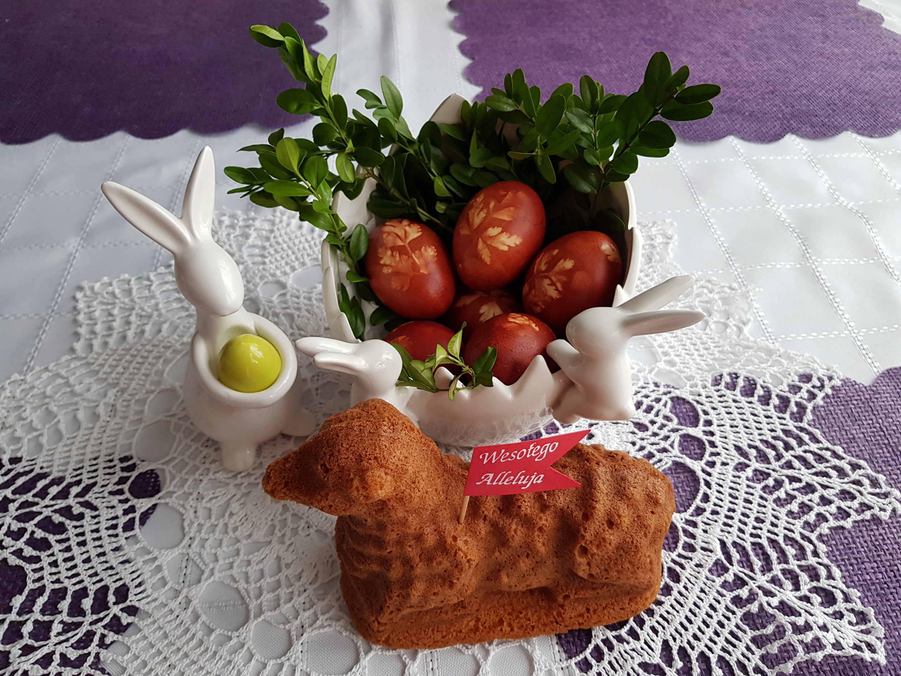Ein gedeckter Tisch hält eine Schüssel mit bunten Ostereiern und Osterhasenfiguren darauf.